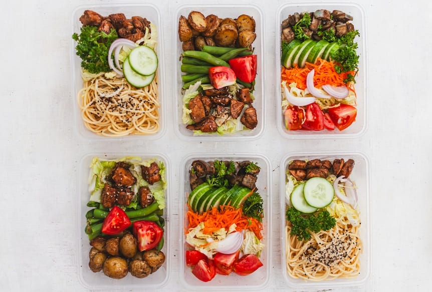 Six meal prep containers with balanced foods—pasta, veggies, grilled chicken—arranged on a white surface for Eat Swim Win’s swim nutrition services for athlete swimmers and their parents. Eat Swim Win