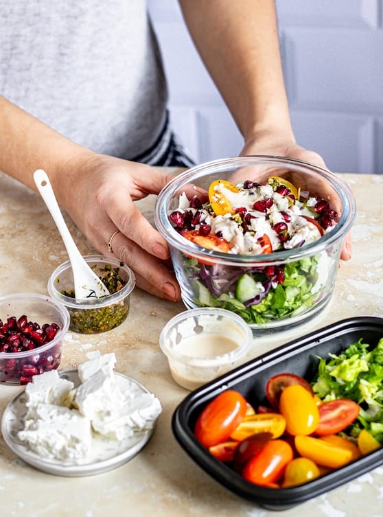 A swimmer or sports dietitian prepares a colorful salad with lettuce, tomatoes, pomegranate seeds, cheese, and dressing—fueling athlete swimmers for peak performance and supporting parents’ nutrition goals. Eat Swim Win